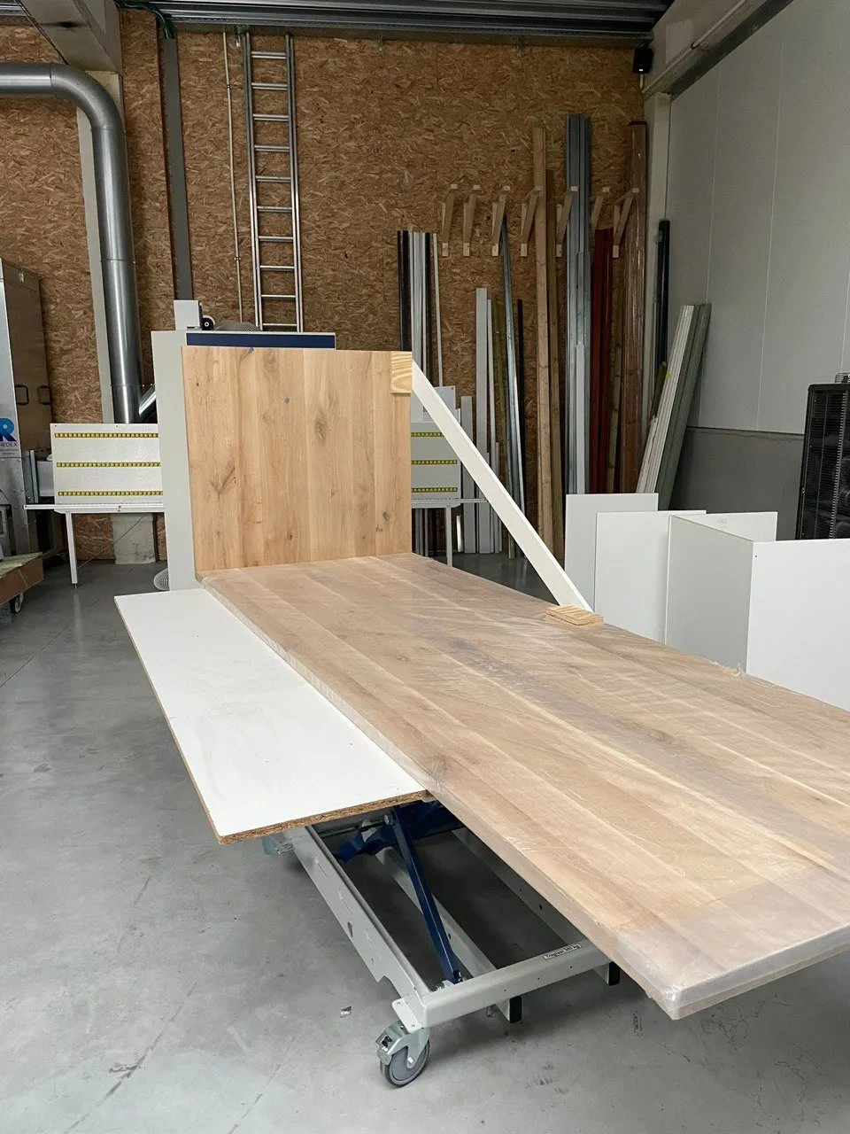 Plan de travail en chêne posé sur un chariot devant la scie à panneaux, à l’atelier d’Evergem