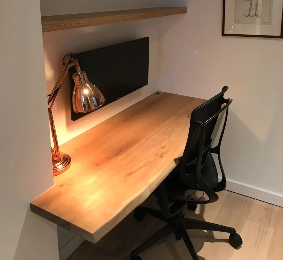 Plateau de bureau en chêne à bord naturel dans une niche, éclairé par une lampe de bureau
