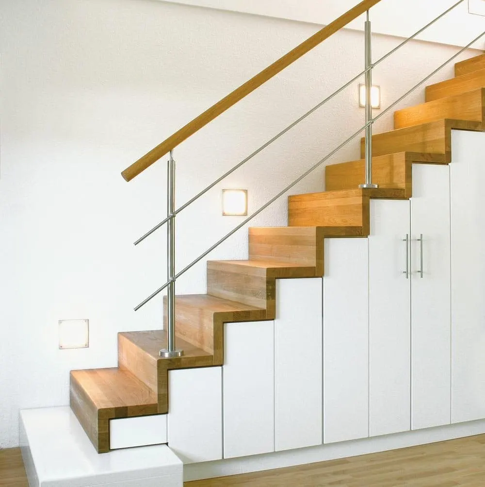 Escalier aux marches et contremarches en chêne au-dessus de placards blancs, avec une main courante